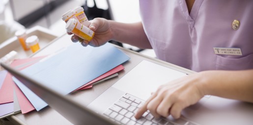 Doctor holding bottle of pills and typing on a computer