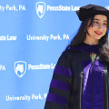 Penn State Law graduate in front of Penn State Law logo